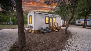 A small, single-story cabin with a porch, a staircase, and a view of the sunset. - Cozy Up with Perfect Private Escape for 2 | Pool + River (New Braunfels)