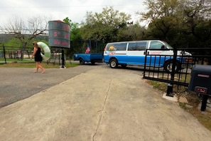 A gated entrance with a blue and white van parked inside, a water tower, and a person walking on the sidewalk. - Bluebonnet Retreat | 1BR King | Hot Tub & Fire Pit (New Braunfels)
