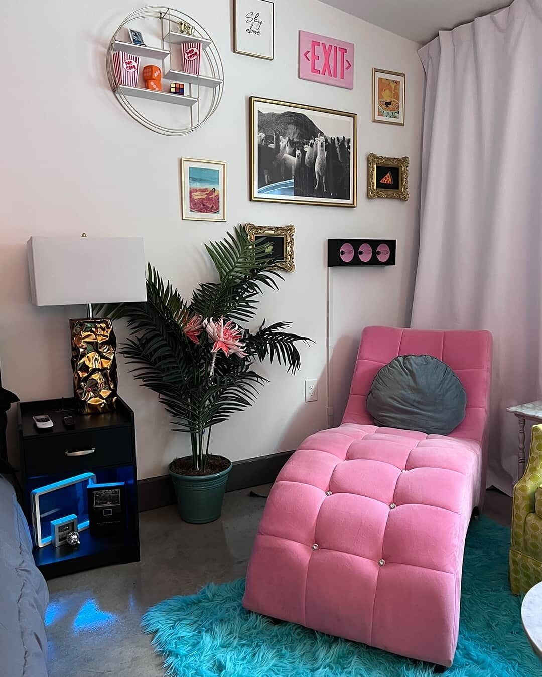 Une chambre à coucher avec un lit rose à capitons, une plante en pot, une étagère fixée au mur et divers tableaux encadrés.
