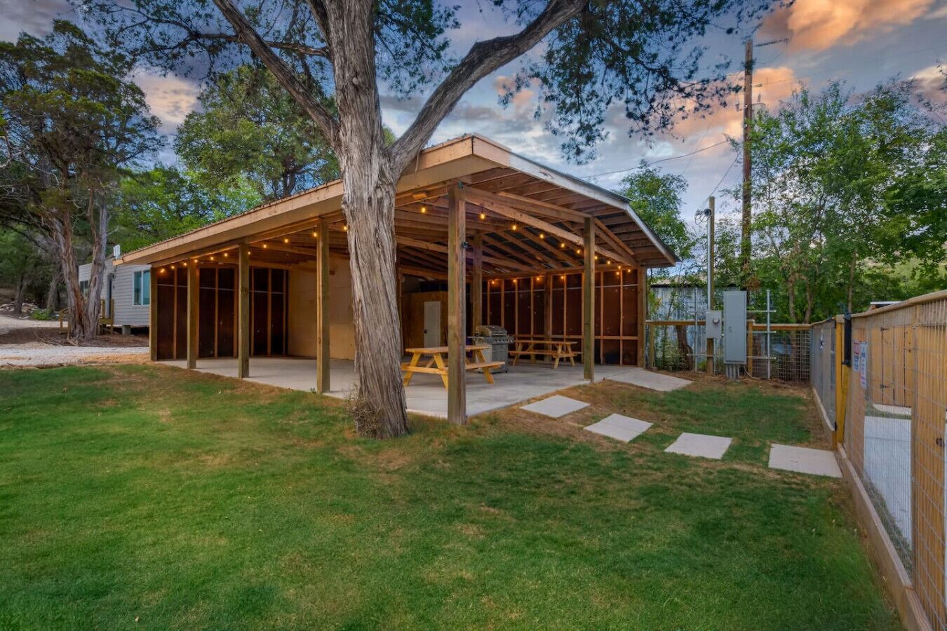 Un patio techado al aire libre con piso de madera, una mesa de picnic y luces colgantes.