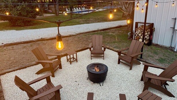 Terassi, jossa on Adirondack-tyylisiä puutarhatuoleja, nuotiopaikka ja valoketju.