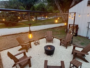 A patio with Adirondack chairs, a fire pit, and string lights. - 5-Star Hill Country Cottage | 2 Kings | Pool + River | Sleeps 6 (New Braunfels)