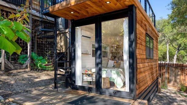 Een moderne houten chalet met een glazen deur, een houten terras en een metalen trap naar een balkon.