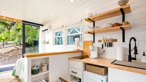 Een compacte keuken met een geïntegreerde koelkast, houten planken en een raam met uitzicht op groen.