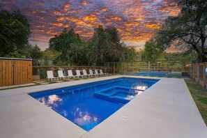 Ein rechteckiger Pool mit Sonnendeck, umzäunt und von Bäumen gesäumt, unter einem Sonnenuntergangshimmel.