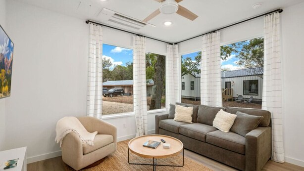 A modern living room with a beige armchair, a gray sofa, and a round coffee table. - Hill Country Cottage | 1BR King | Pool + Hot Tub | Pets Welcome (New Braunfels)