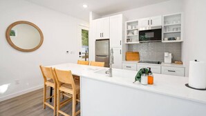 A modern kitchen with white cabinetry, a central island, and a round mirror. - Hill Country Cottage | 1BR King | Pool + Hot Tub | Pets Welcome (New Braunfels)