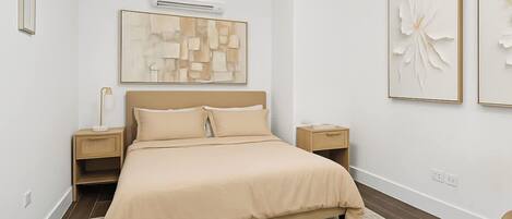 A modern bedroom with a bed, two bedside tables, a wall-mounted air conditioner, and abstract wall art.