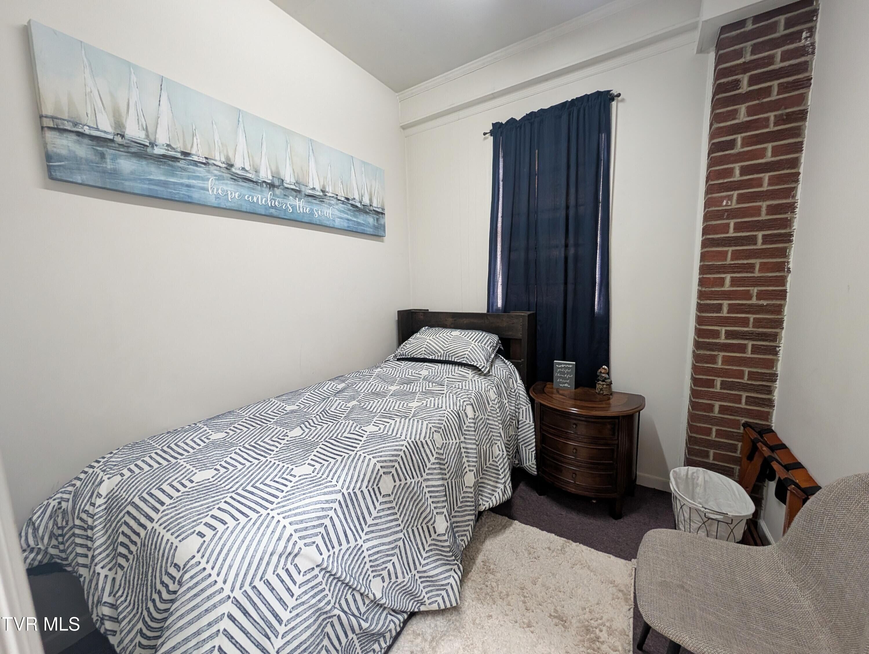 Een slaapkamer met een bed, een kaptafel, een stoel, een vloerkleed, een schilderij en een bakstenen muur.