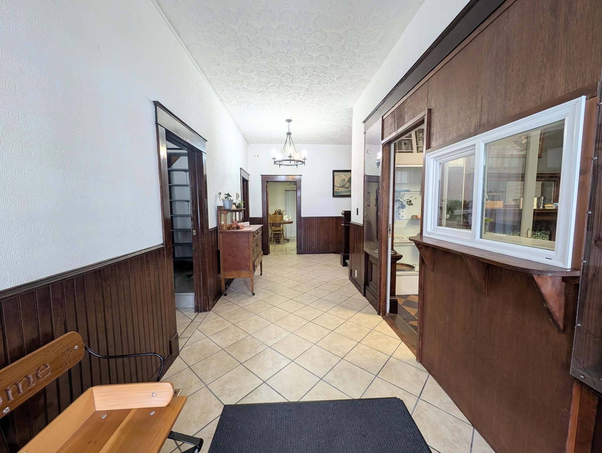A hallway with wooden paneling, a bench, a tiled floor, and a door leading to a room with a window.