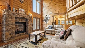 A log cabin interior with a stone fireplace, leather sofa, and a large window.