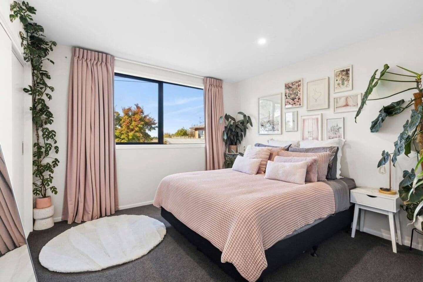 Un dormitorio con una cama grande, una mesita de noche, una ventana con cortinas y varias fotografías en la pared.