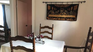 Een eetruimte met een tafel gedekt voor vier personen, houten stoelen, een schilderij van 'The Last Supper' aan de muur en een deur die naar een andere kamer leidt.