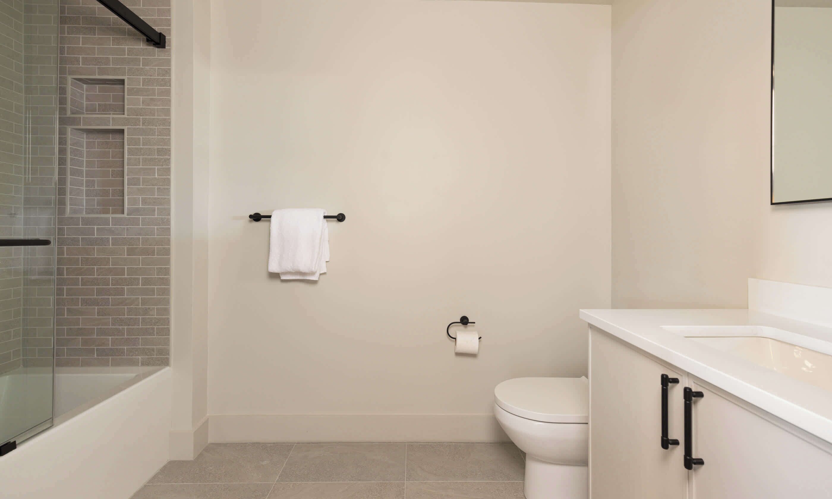Een moderne badkamer met een douchecabine van glas, een wit toilet en een witte wastafel met zwarte handgrepen.