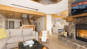 A spacious living area with a high ceiling, wooden beams, a stone fireplace, a sofa, a coffee table, and a staircase leading to an upper level. - *New to Market* 5 Bedroom Big Sky Resort Condo (Big Sky)