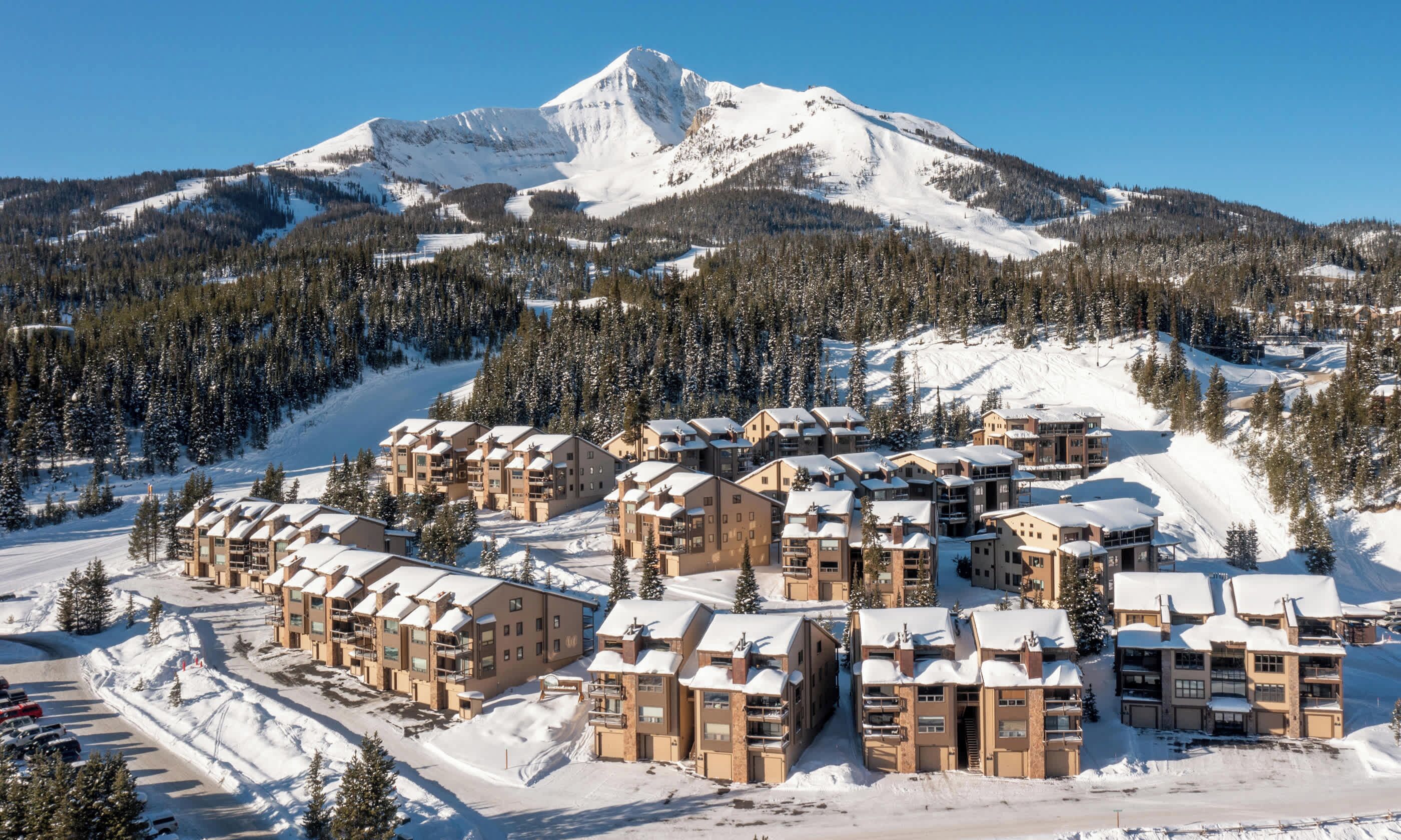 Une station de ski enneigée, composée de plusieurs bâtiments, de pistes de ski et avec une montagne en toile de fond.