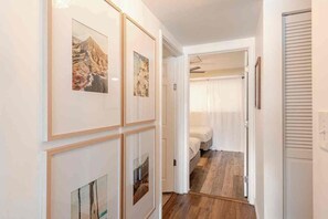 Un pasillo con cuadros en la pared, una cama en la habitación contigua y suelo de madera.