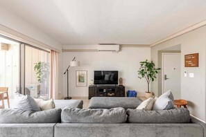 Una sala de estar moderna con un sofá gris, un televisor de pantalla plana, una lámpara de pie y una planta en maceta.