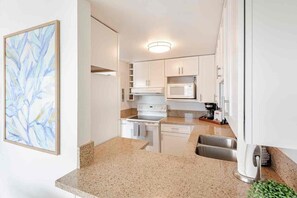Cocina compacta con armarios blancos, microondas, cafetera y encimera de granito.