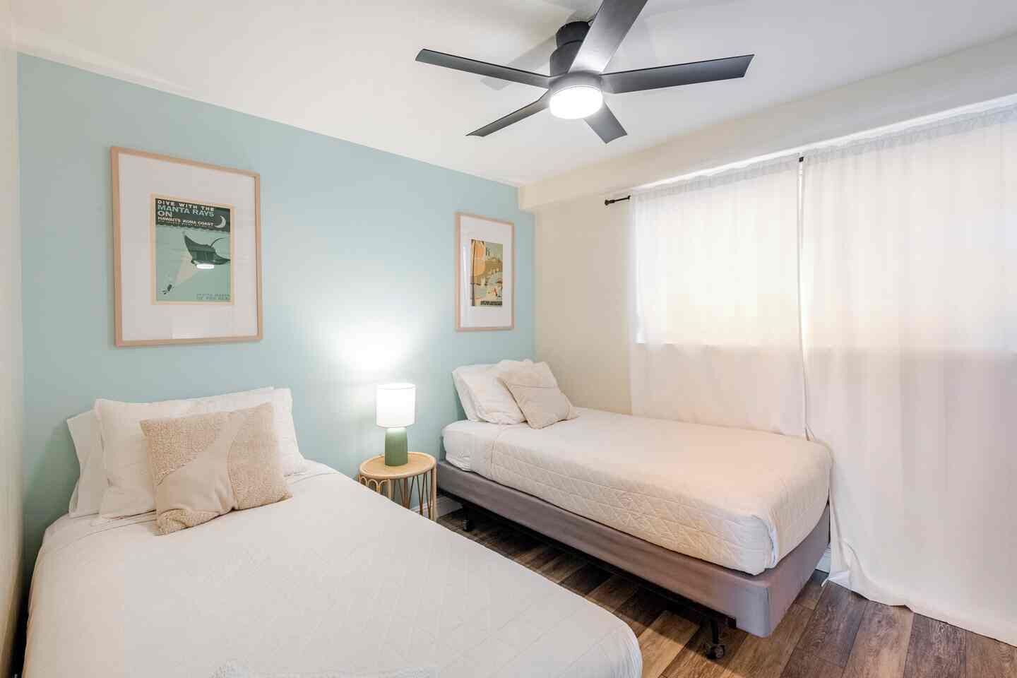 A hotel room with two beds, a ceiling fan, and two framed posters on the wall.