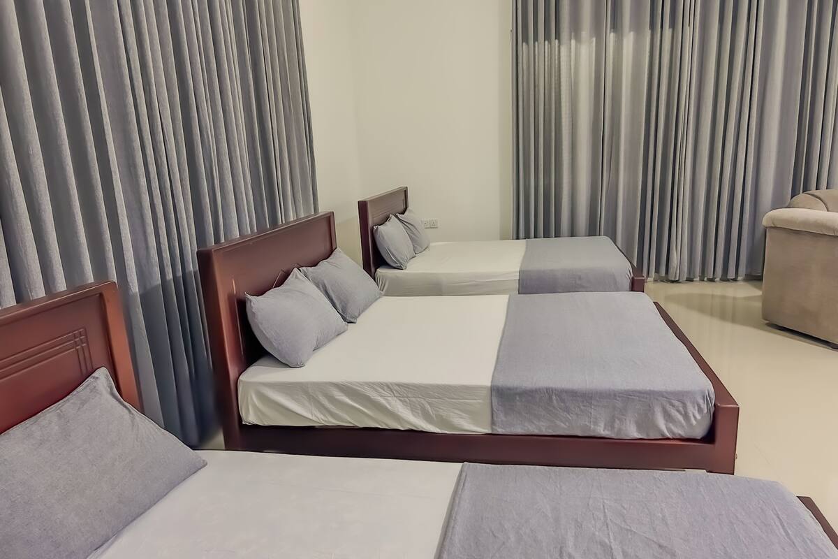 Et hotelværelse med tre enkeltsenge, hver med en træsenggavl og gråt sengetøj.
