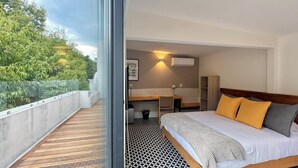 Quarto de hotel com cama, secretária e banheiro. Possui uma varanda com vista para árvores.