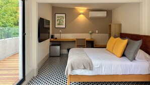 Quarto de hotel com cama, escrivaninha e pequena cozinha equipada.