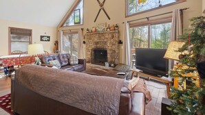 A cozy living room with a stone fireplace, large windows, a television, and a Christmas tree. - Family-Friendly Home w/ Hot Tub • Fire Pit• Games (Swanton)