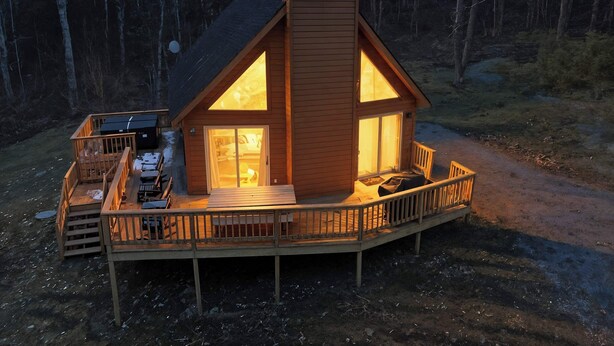 A cabin with a deck, a chimney, and a large window. - Family-Friendly Home w/ Hot Tub • Fire Pit• Games (Swanton)