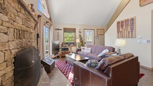 A cozy living room with a stone fireplace, a leather sofa, a television, and a red patterned rug. - Family-Friendly Home w/ Hot Tub • Fire Pit• Games (Swanton)