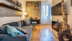 Una sala moderna con sofá, una mesa de centro y televisor. Hay una estantería y una planta decorativa.