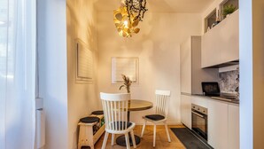 Una cocina moderna con comedor, que incluye una mesa redonda, dos sillas blancas, un taburete pequeño, una lámpara colgante y un horno empotrado.