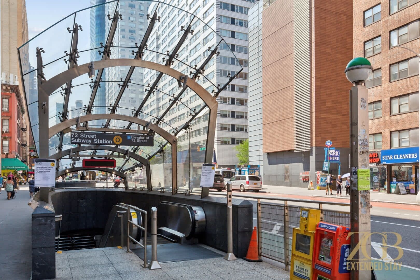 Entree van een stedelijk metrostation met een glazen overkapping, een bord met daarop 72 Straat Metrostation, en een zichtbare lift.