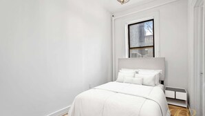 A modern bedroom with a large bed, a window, and a radiator. - Sun-Filled Brownstone Apt in Prime Chelsea (New York)
