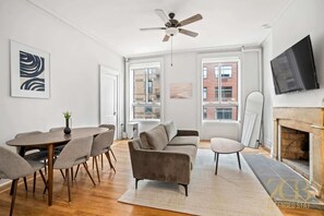 A modern living room with a dining area, a fireplace, and large windows. - Sun-Filled Brownstone Apt in Prime Chelsea (New York)