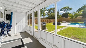 Eine überdachte Veranda mit Blick auf einen Garten, der einen Pool, einen Grill und Liegestühle zeigt.