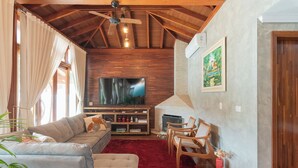Ein gemütliches Wohnzimmer mit Holzbalkendecke, einem großen Flachbildfernseher, einem Kamin und einem roten Teppich.