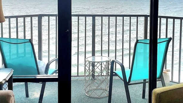 Ein Balkon mit türkisfarbenen Stühlen und einem kleinen Tisch mit Blick aufs Meer.