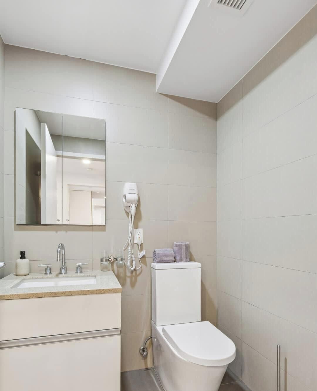 Un baño moderno con lavamanos, espejo e inodoro blancos.