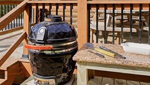 A black barbecue grill with a control panel, a red handle, and a spatula on a wooden deck. - Newly Refreshed : Knotty Pine Cabin + Hot Tub (Logan)