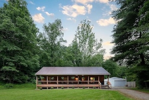 A wooden cabin with a porch, surrounded by trees. - Newly Refreshed : Knotty Pine Cabin + Hot Tub (Logan)