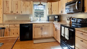 A kitchen with wooden cabinets, a microwave, a dishwasher, and a stove. - Newly Refreshed : Knotty Pine Cabin + Hot Tub (Logan)