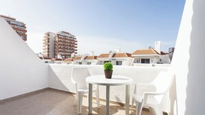 A rooftop terrace with a round table and white chairs, a potted plant, and a view of surrounding buildings. - Home2Book Relax & Enjoy in Las Americas (Playa de la Américas)