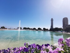 Un cielo azul despejado, una fuente y un monumento en una plaza pública.