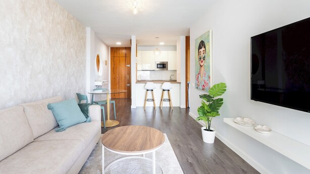 Ein modernes Wohnzimmer mit einer Couch, einem runden Couchtisch und einem an der Wand montierten Fernseher.