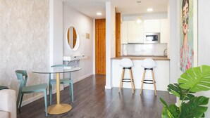 Una cucina moderna con mobili bianchi, un forno a microonde e una porta in legno. In primo piano, un tavolo rotondo con sedie e una pianta grande.