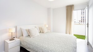 Ein modernes Hotelzimmer mit einem großen Bett, einem Nachttisch mit Lampe und Blick auf eine grüne Rasenfläche durch ein großes Fenster.