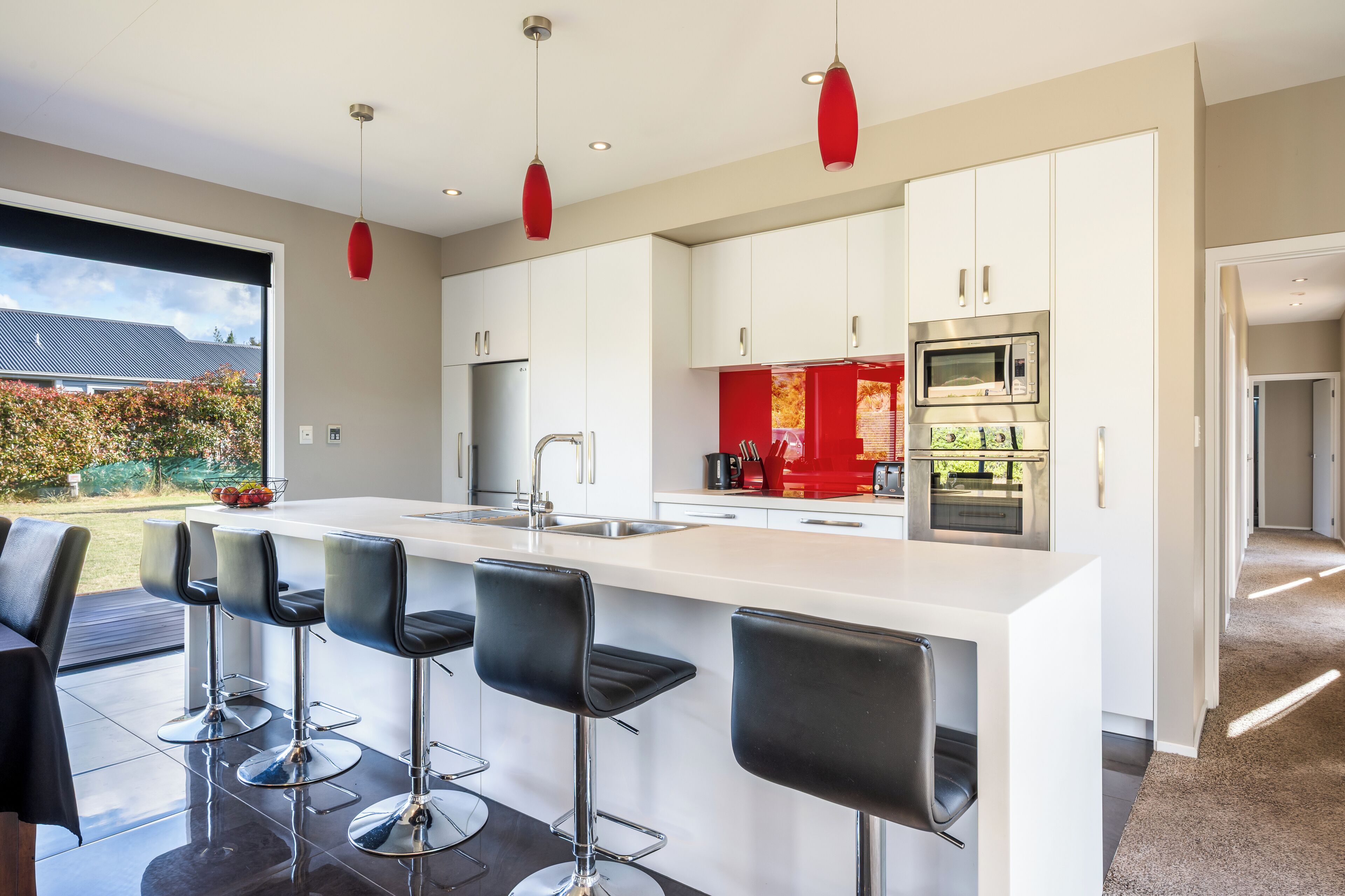 Una cocina moderna con armarios blancos, electrodomésticos de acero inoxidable y una isla central con taburetes de bar.
