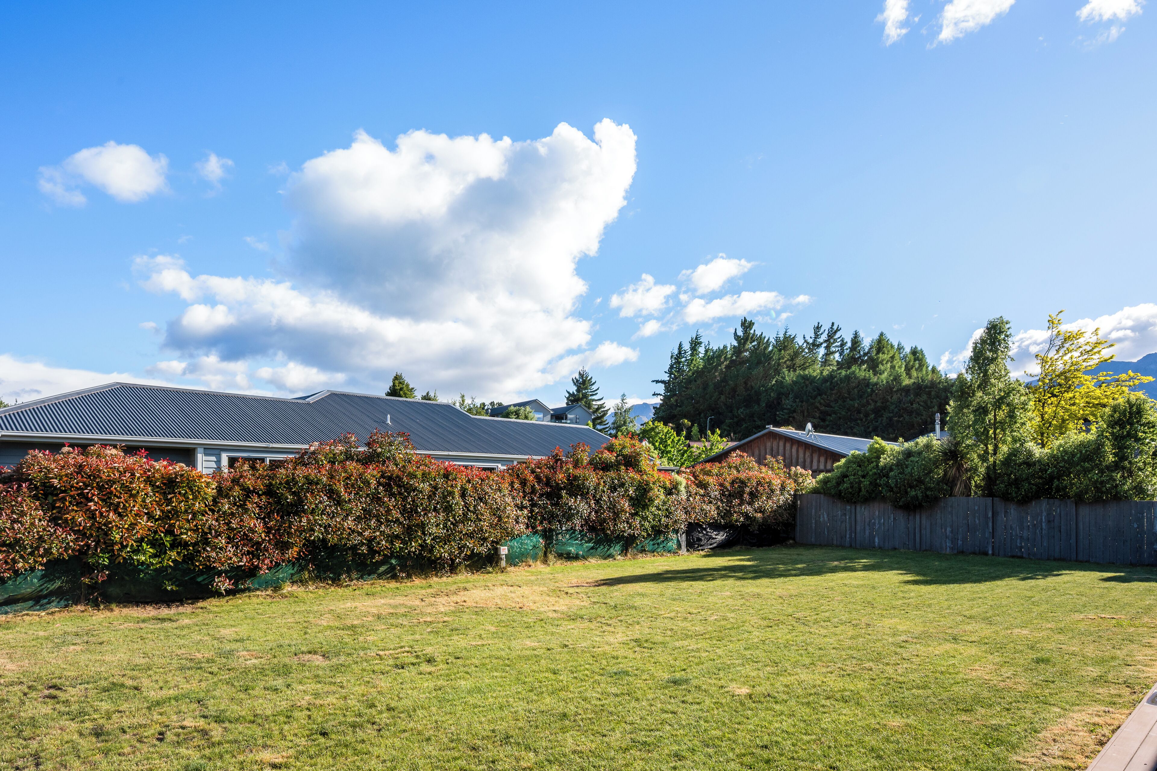 A residential backyard with a lawn, a wooden fence, and a house with a sloped roof.