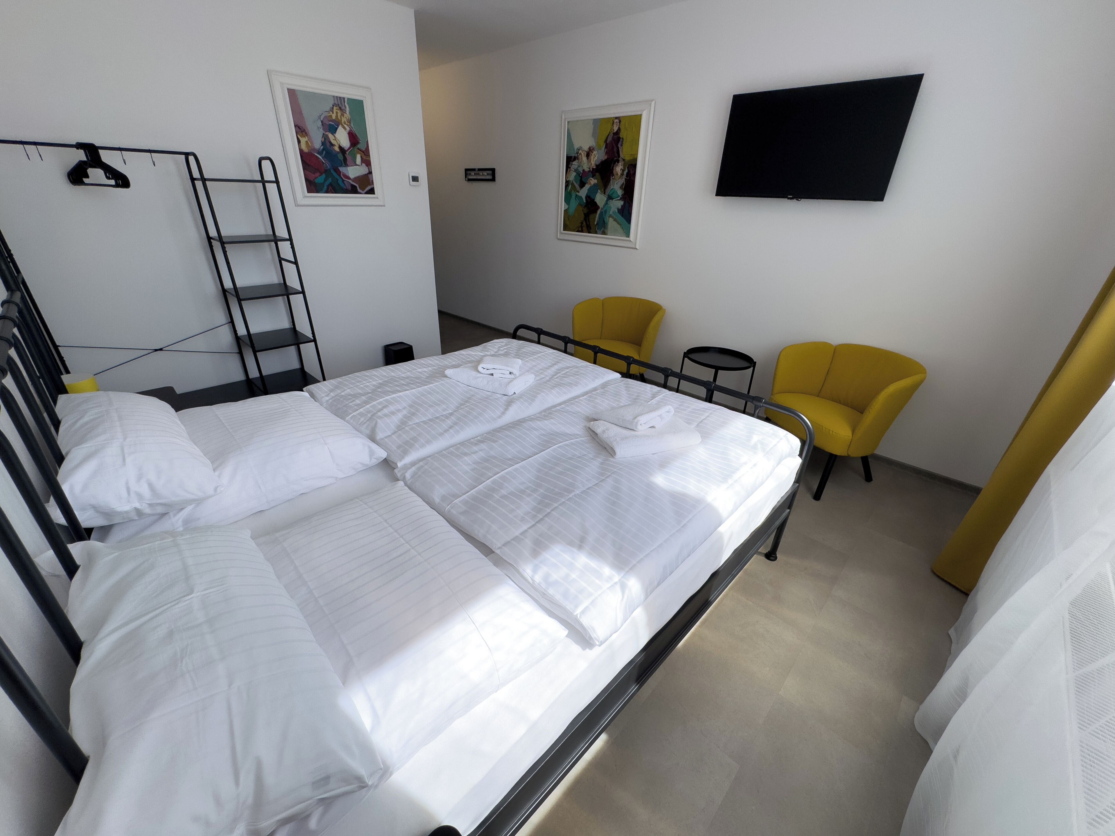 A hotel room with a bed, two yellow chairs, a TV, and artwork on the walls.